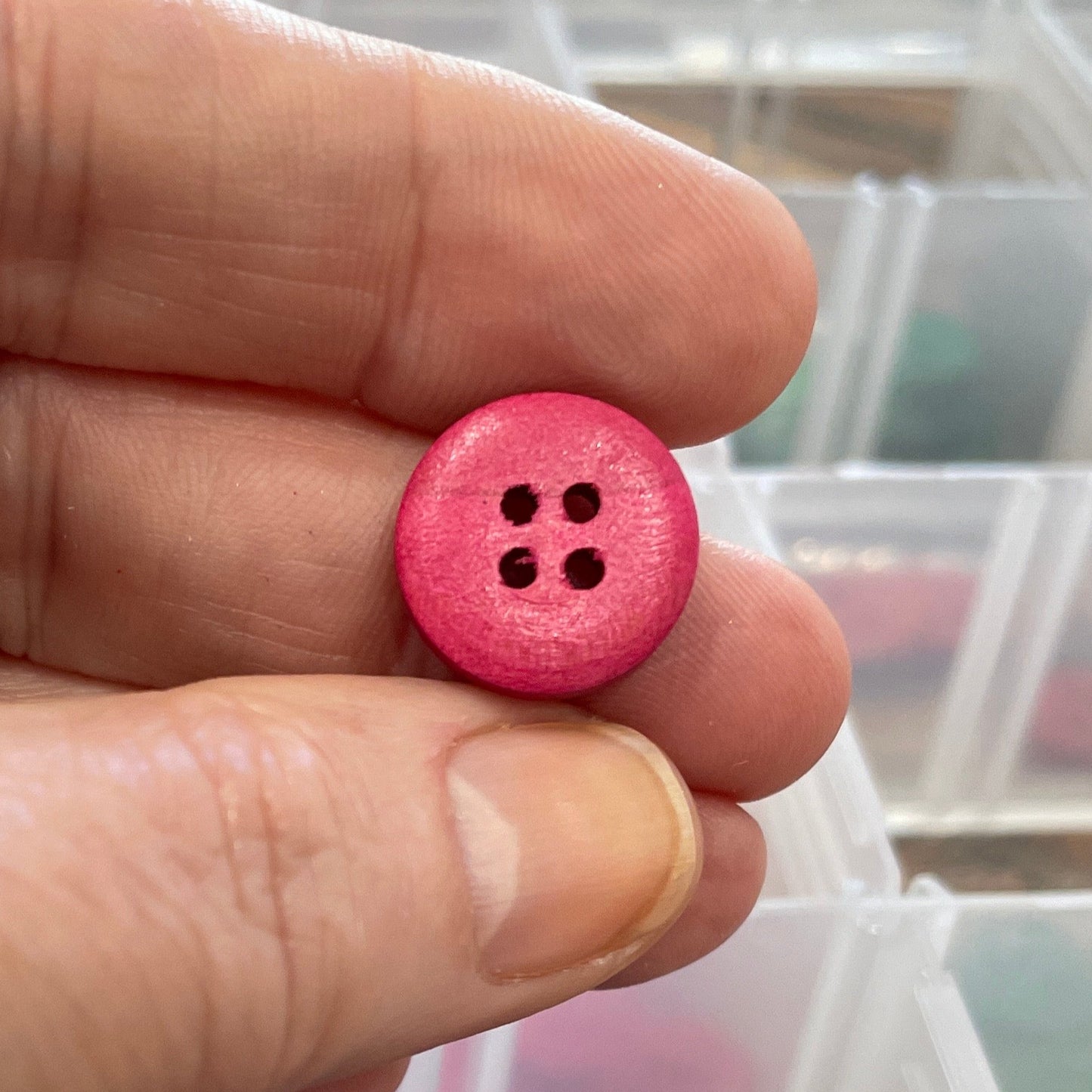 Hand holding a pink button with a container of buttons in the background