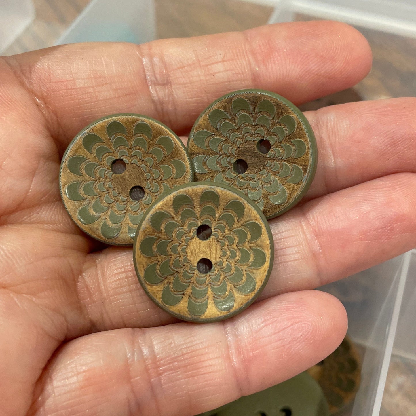 Hand holding three decorative buttons with a clear container of more buttons in the background