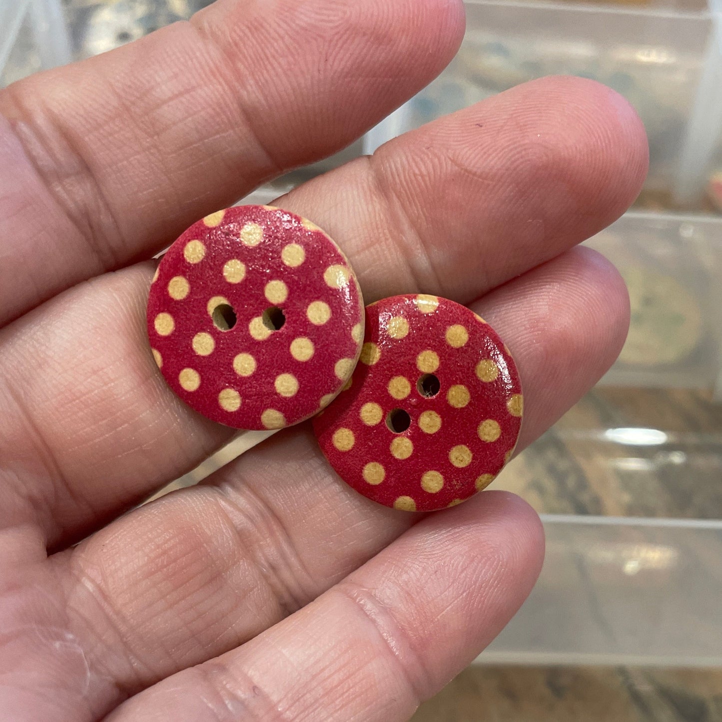 Hand holding two red buttons with yellow polka dots in front of a clear plastic organizer.