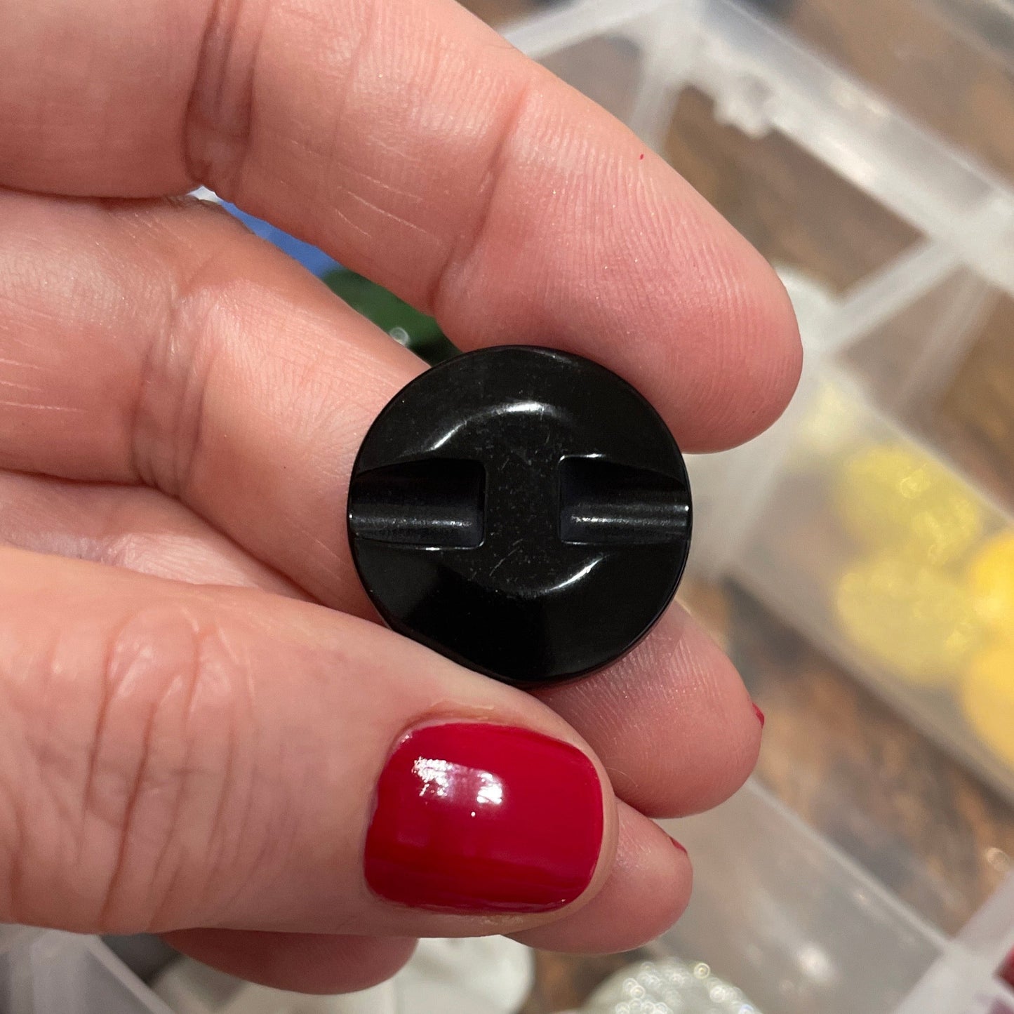 Hand holding a black button with a container of various buttons in the background