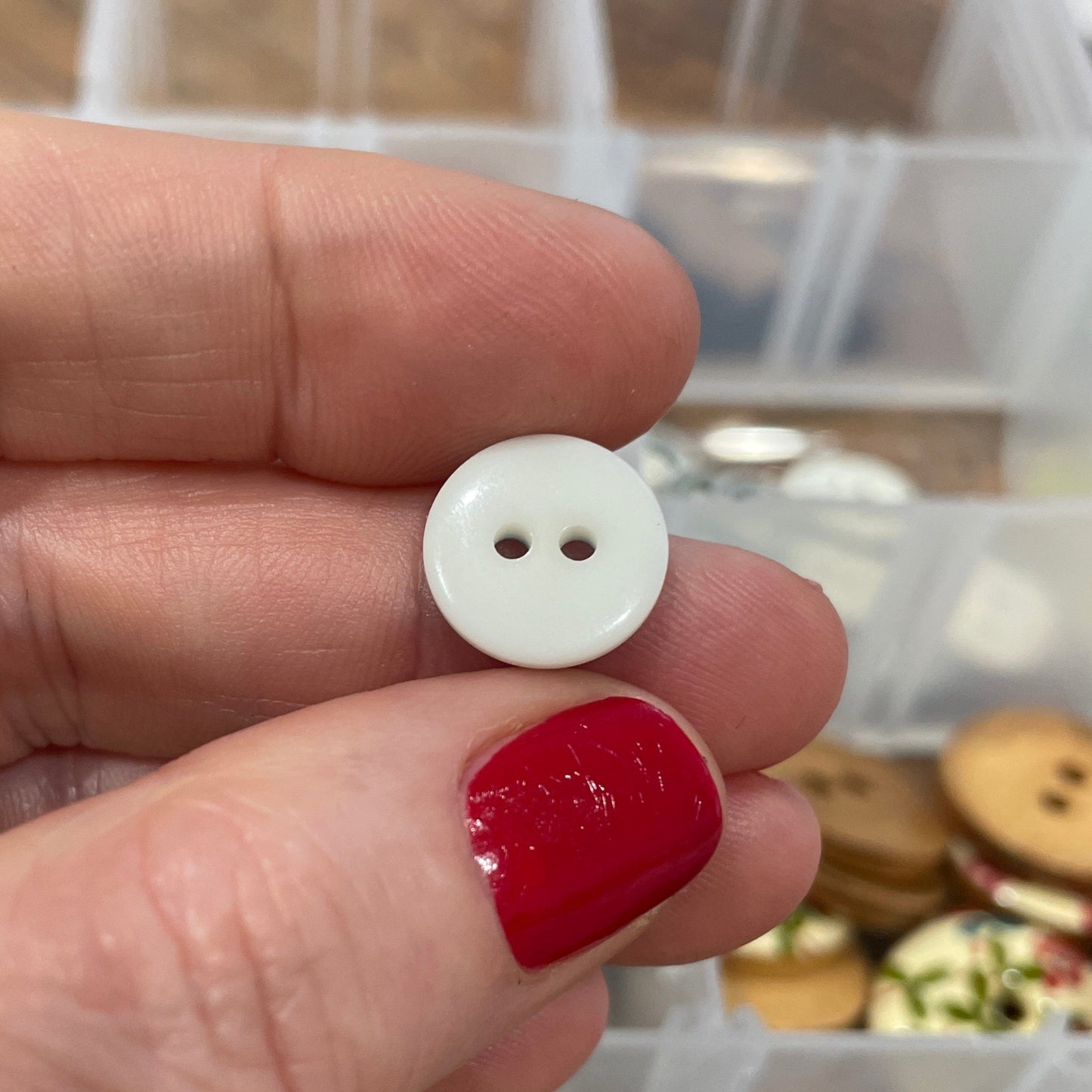 Hand holding a small white button with a container of buttons in the background