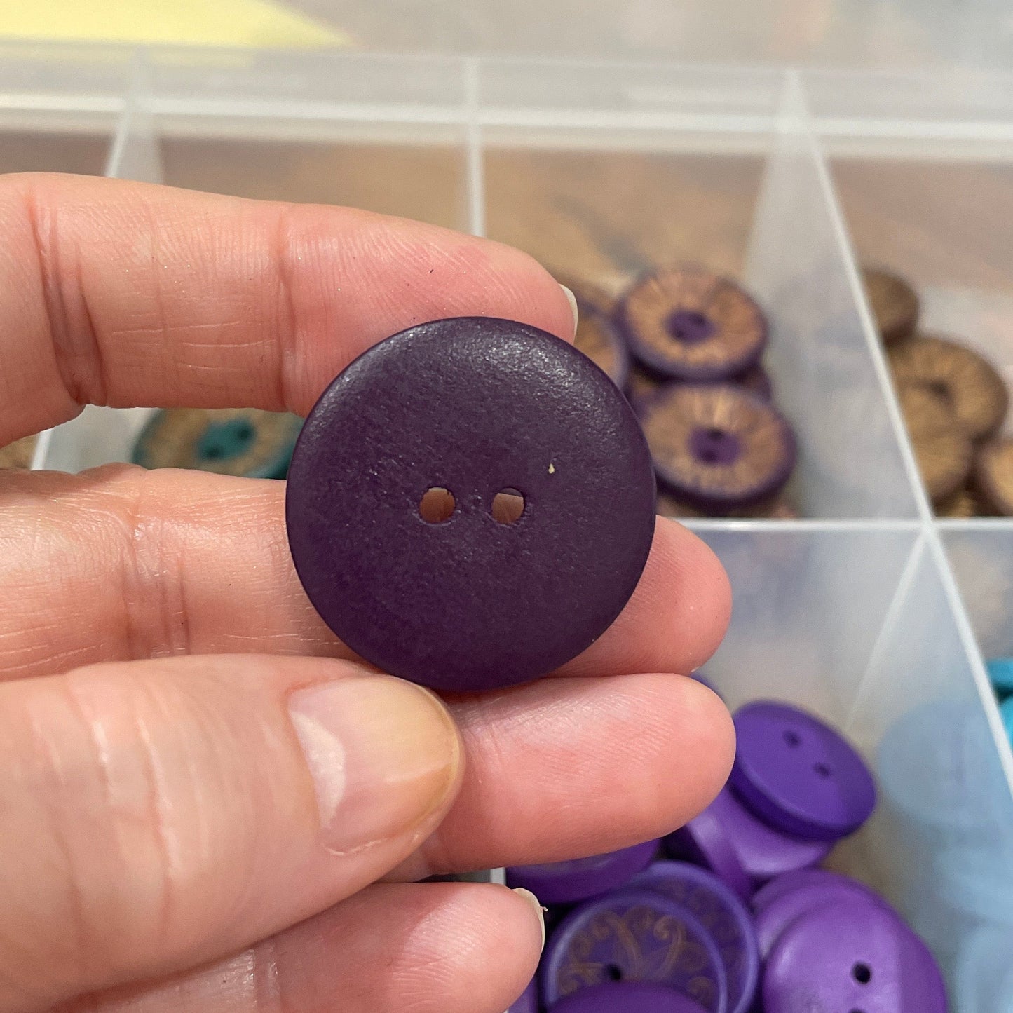 Hand holding a purple button with a container of buttons in the background