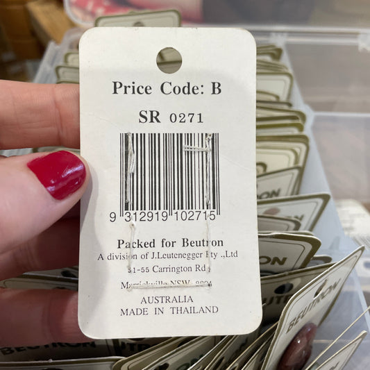 Close-up of a price tag with a barcode and text, held by a hand with red nail polish.
