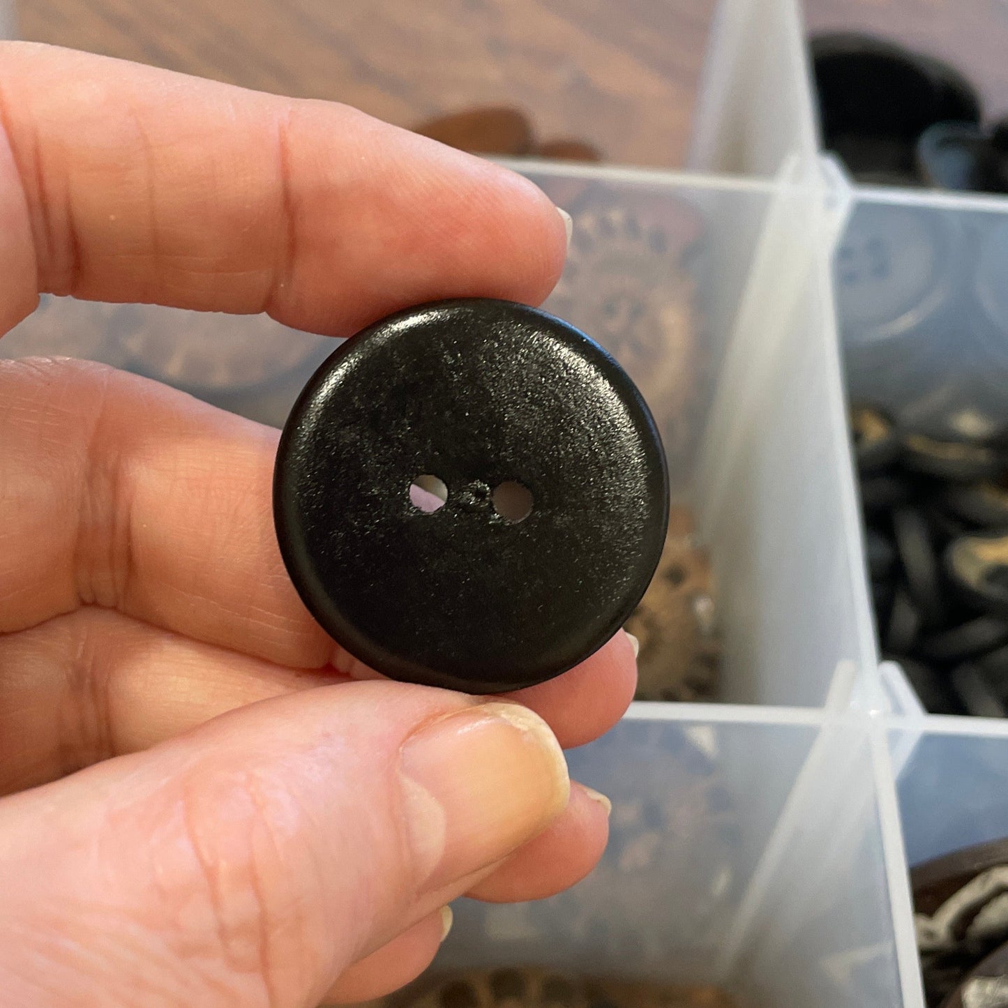 Hand holding a black button with a clear container of buttons in the background