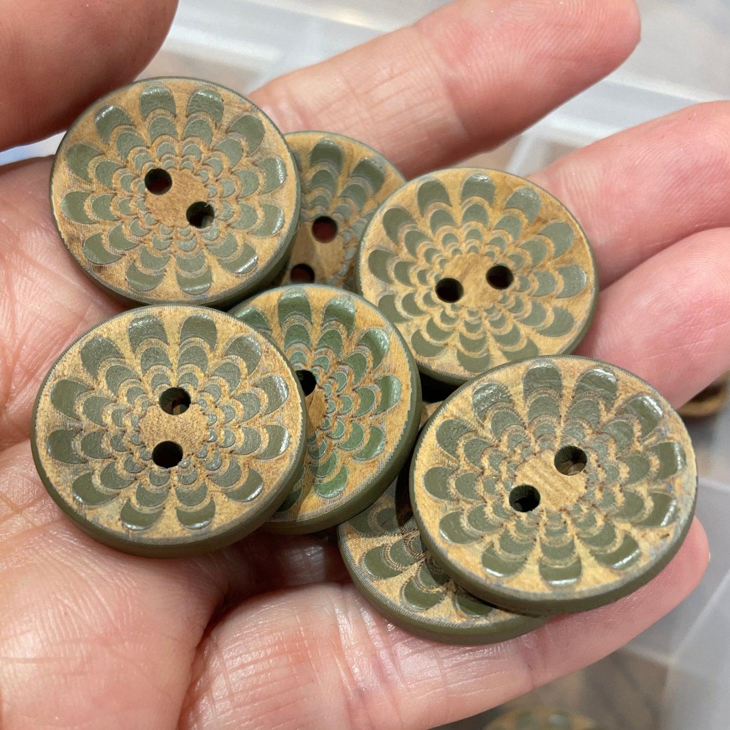 Hand holding a collection of green ceramic buttons with intricate patterns.