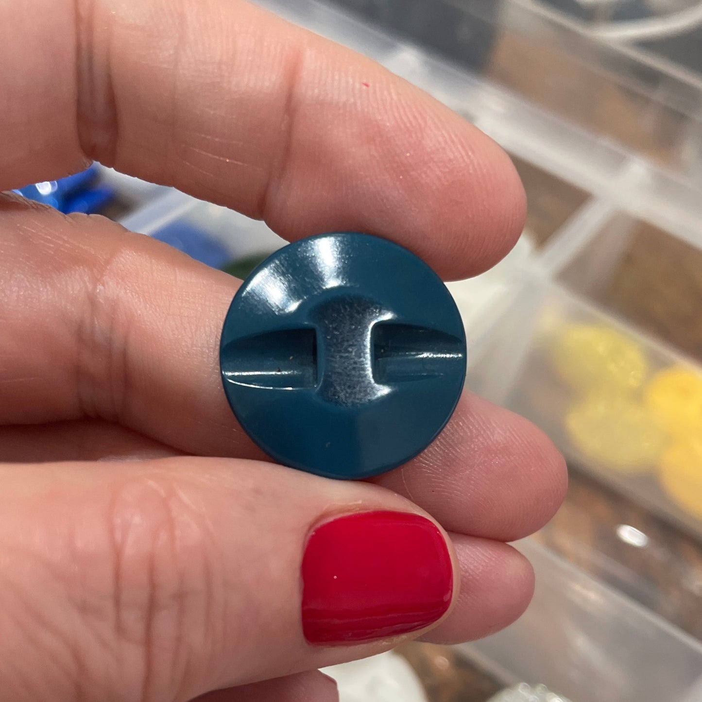 Hand holding a blue plastic component with a clear container of various items in the background