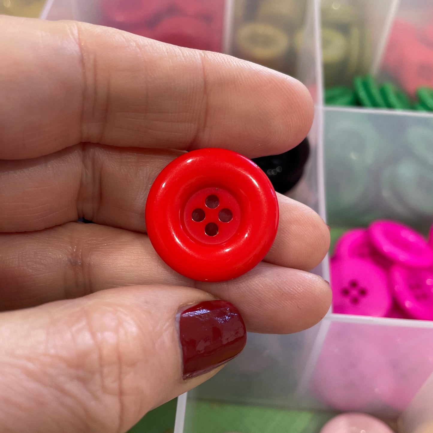 Hand holding a red button with a background of various buttons in containers