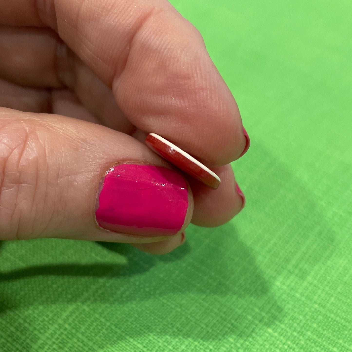 Hand with pink nail polish holding a small object against a green background