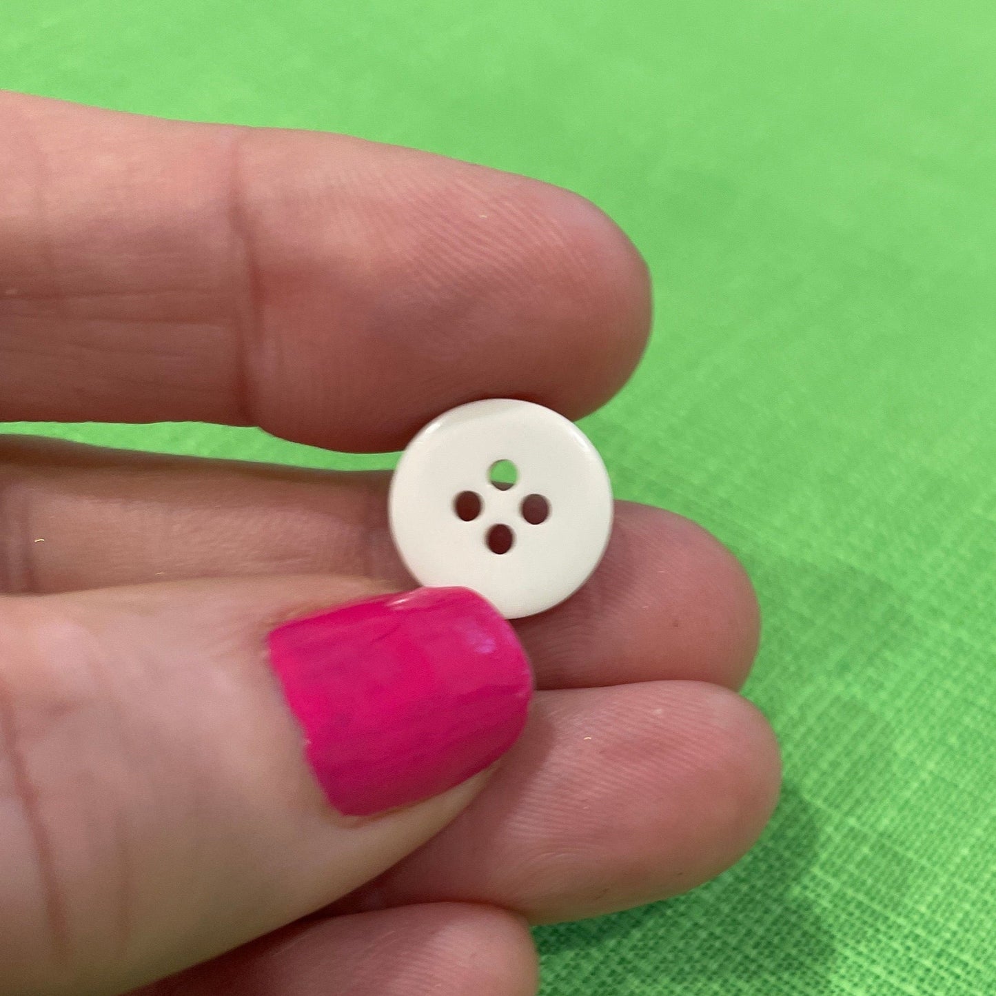 White button held between thumb and forefinger against a green background