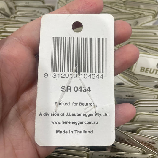 Hand holding a product tag with a barcode and text, with a blurred background of similar tags.