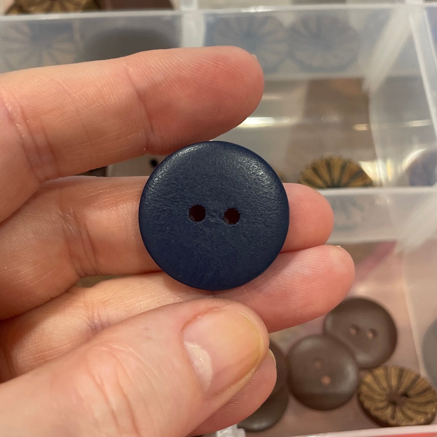 Hand holding a black button with a clear container of assorted buttons in the background