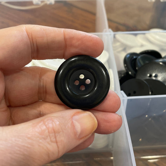 Hand holding a black button with a clear container of buttons in the background