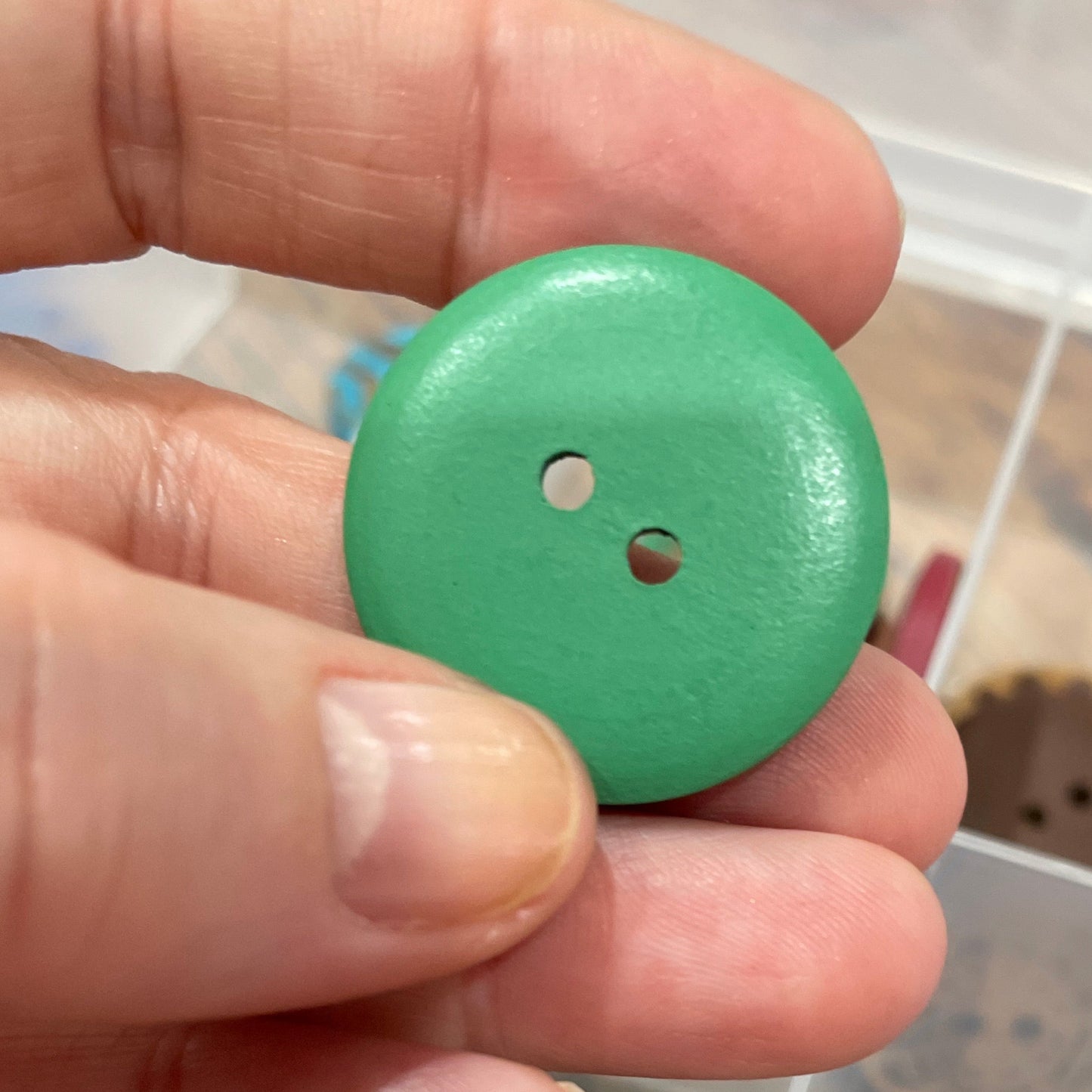 Hand holding a green button with a collection of decorative buttons in the background.