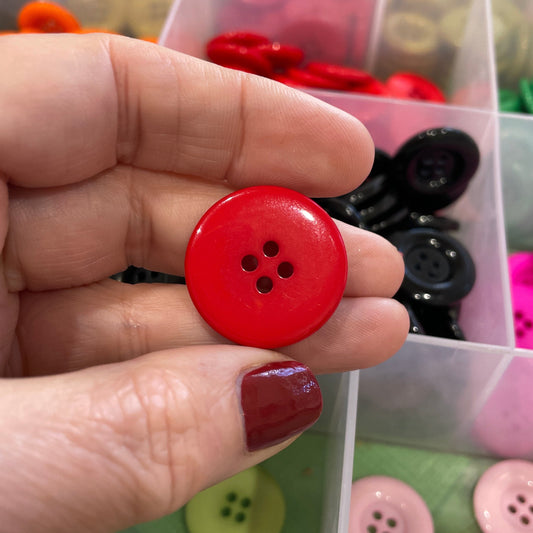 Hand holding a red button with a background of colorful buttons in a box
