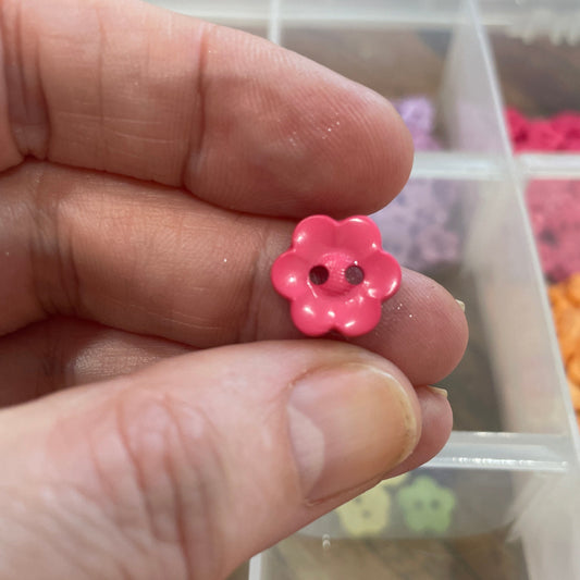 Hand holding a pink flower-shaped earring with a blurred background of jewelry boxes.