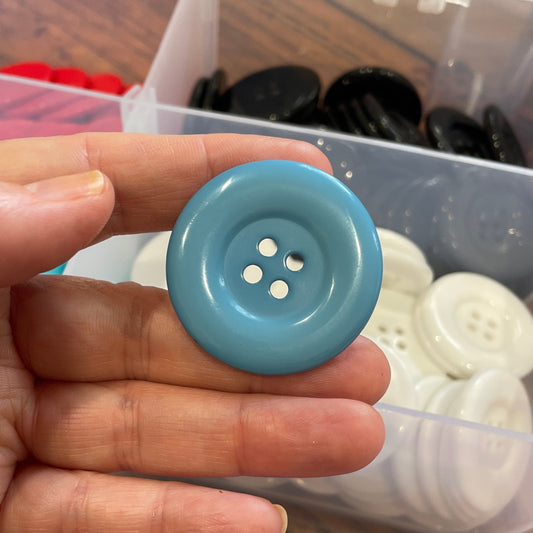 Hand holding a blue button with a container of buttons in the background