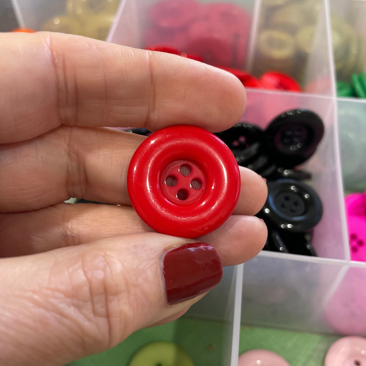 Hand holding a red button with a background of assorted buttons in a container