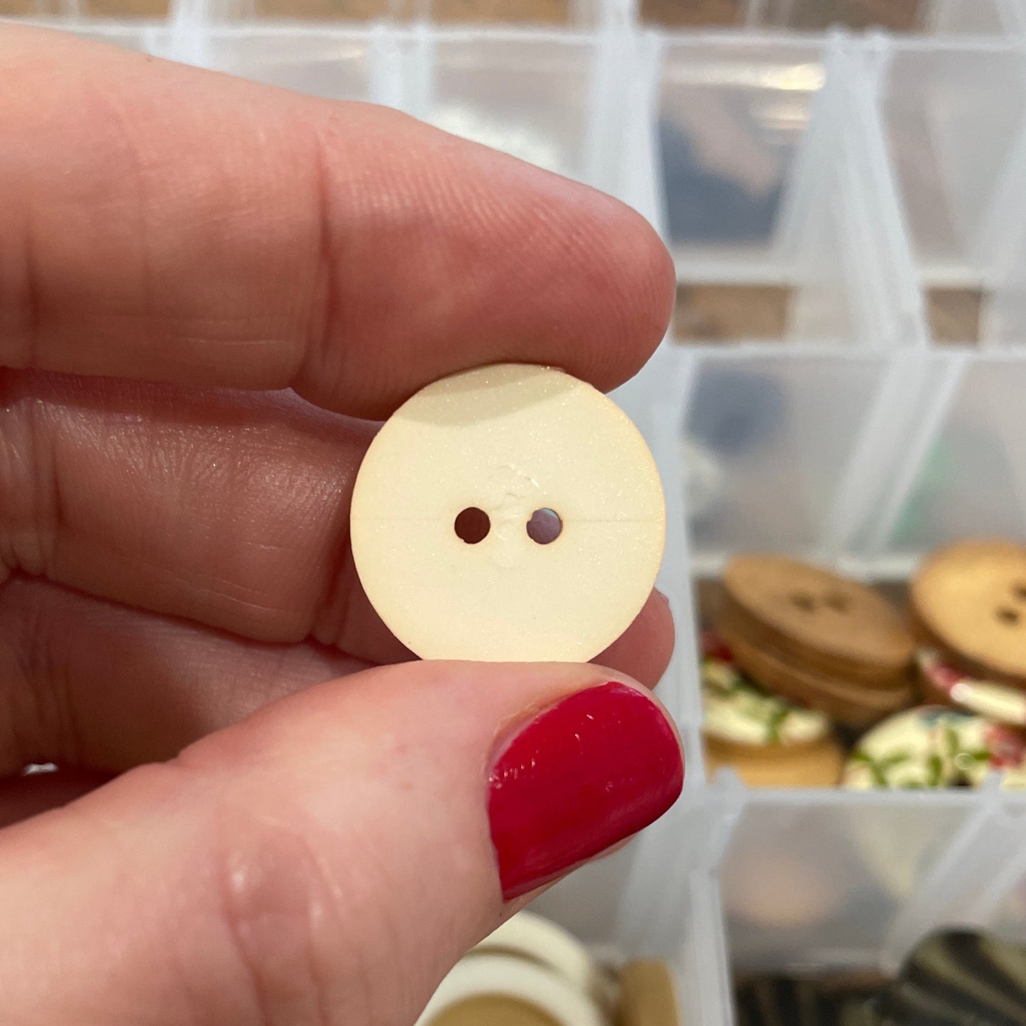 Hand holding a beige button with a container of buttons in the background