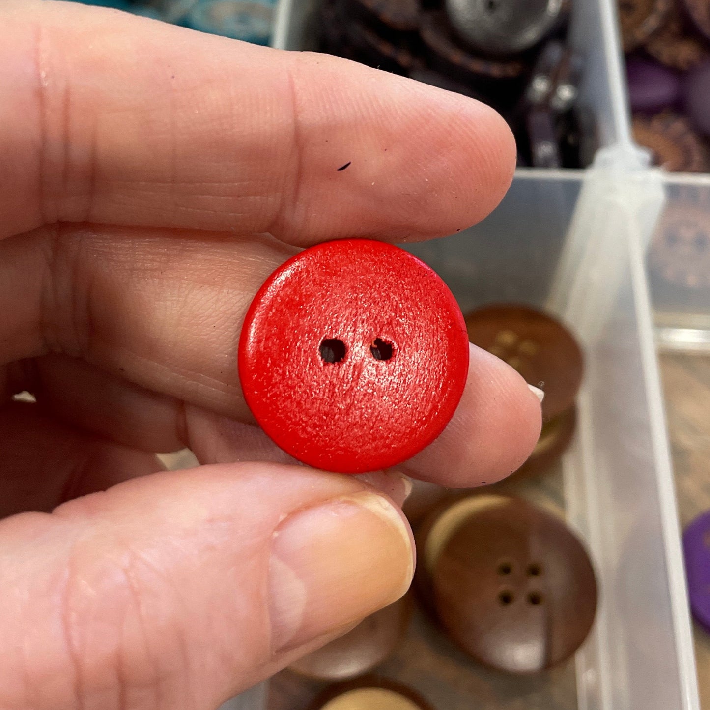 Hand holding a red button with a container of various buttons in the background