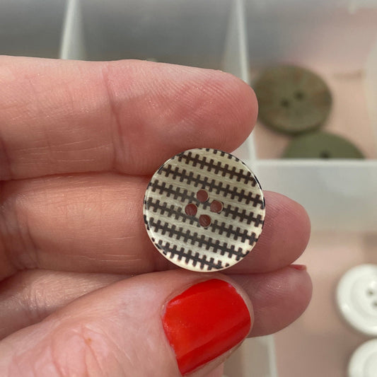 Hand holding a button with a textured pattern in front of a container of buttons.