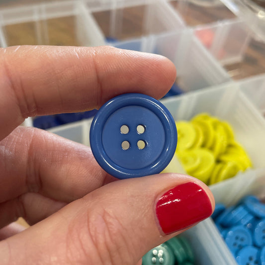 Hand holding a blue button with a blurred background of colorful buttons