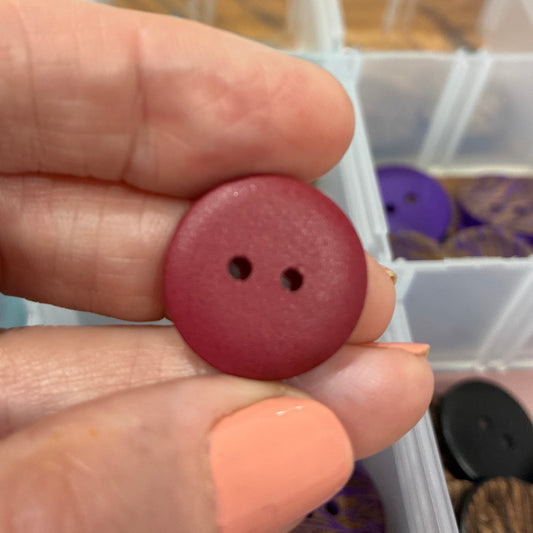 Hand holding a red button with a clear container of buttons in the background