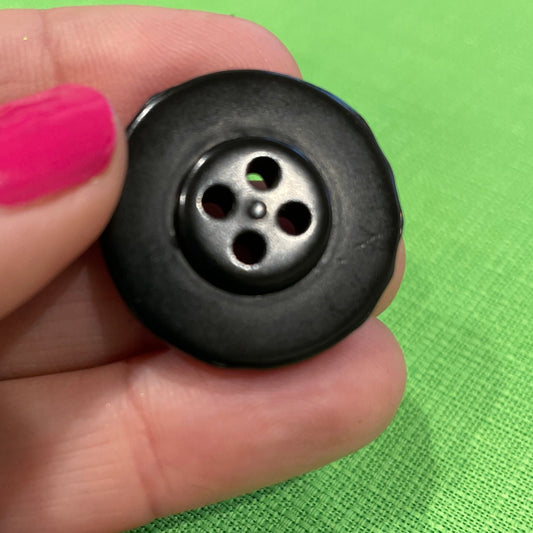 Black button held between fingers against a green background