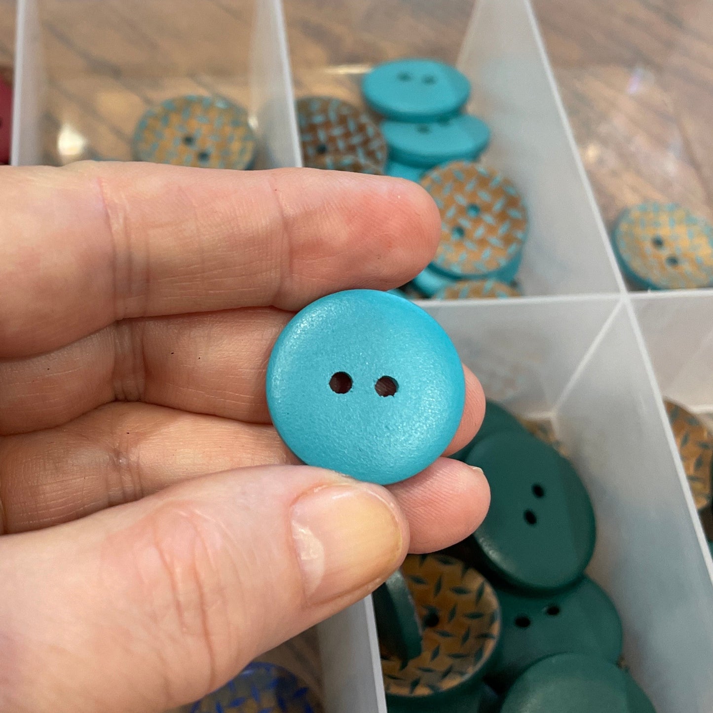 Hand holding a blue button with a container of assorted buttons in the background