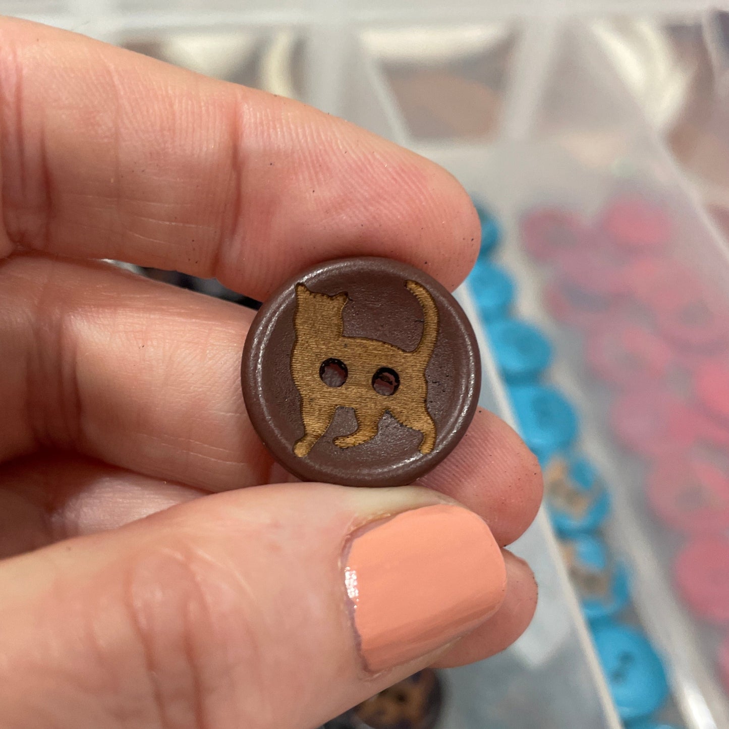 Hand holding a brown button against a background of a button collection in a box.