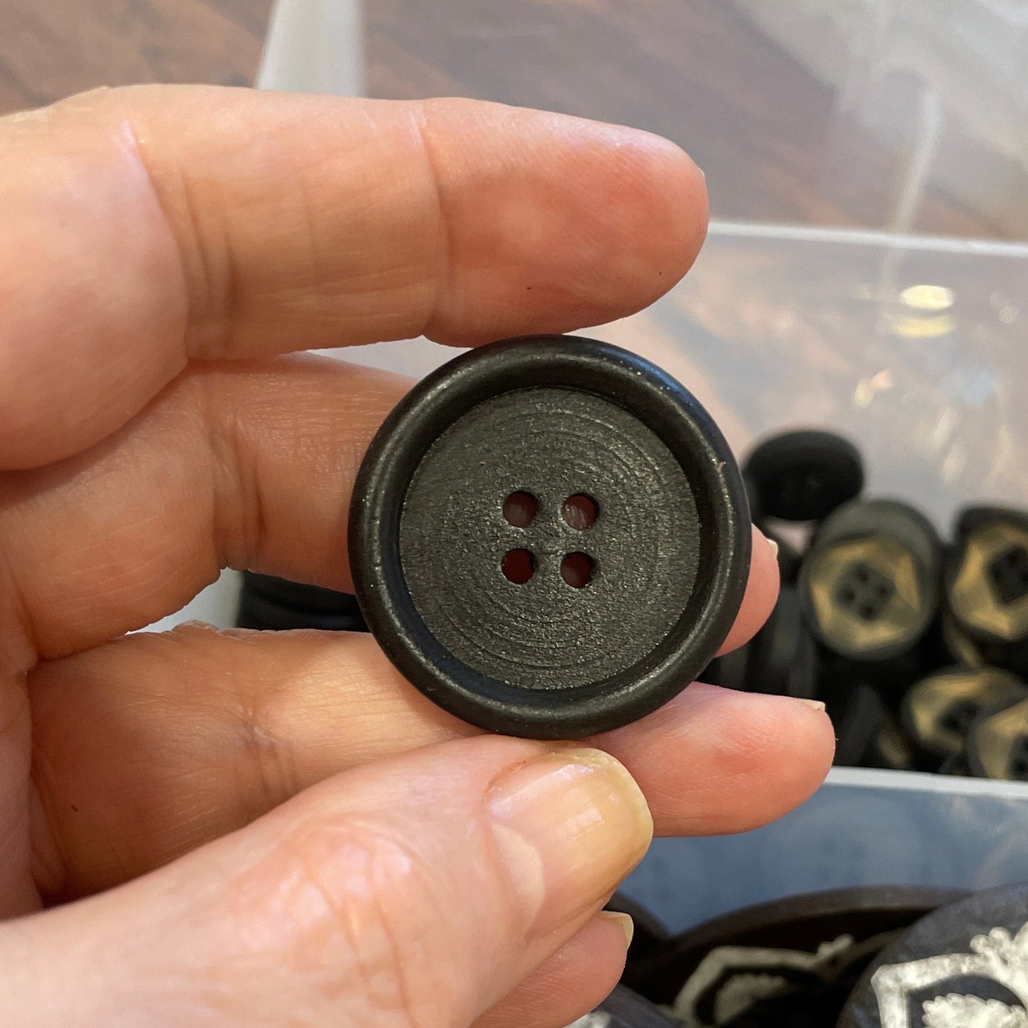 Hand holding a black button in a container of buttons.