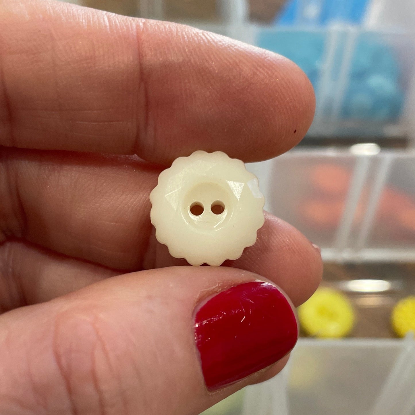 White button held between fingers with a container of buttons in the background