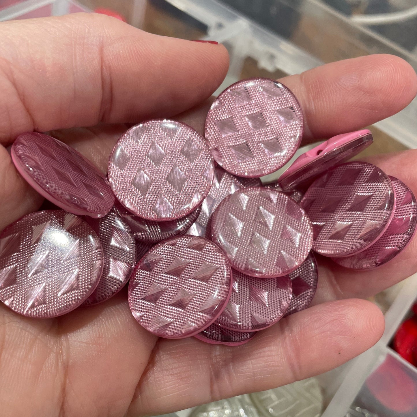 Hand holding pink textured buttons with a container of various buttons in the background