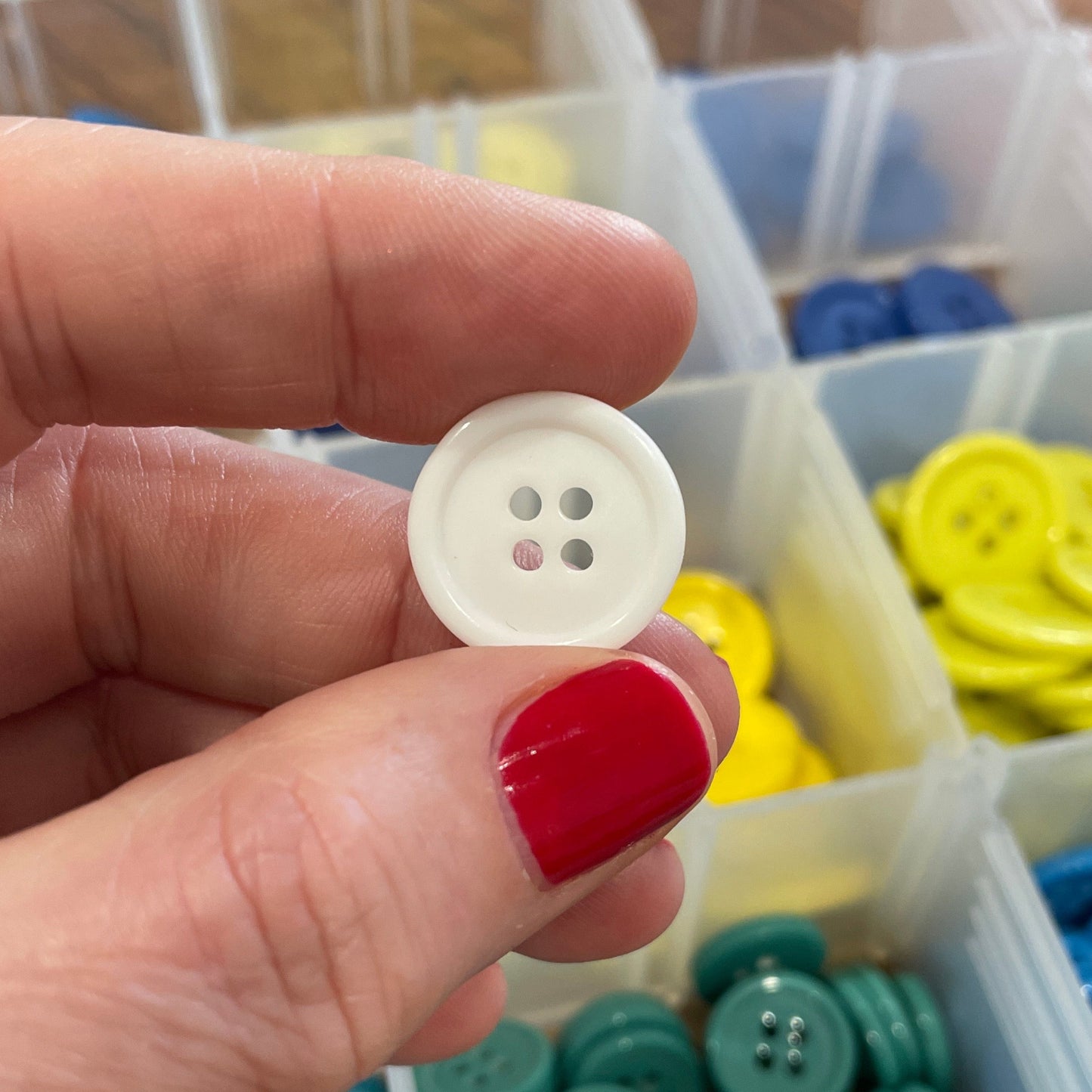Hand holding a white button with a container of colorful buttons in the background