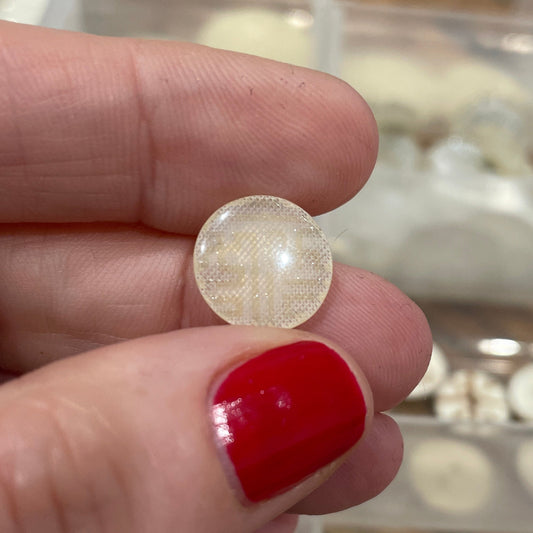 Hand holding a round pearl earring with a blurred background of more earrings in cases.