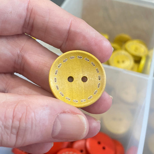 Hand holding a yellow button with a container of colorful buttons in the background