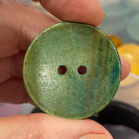 Hand holding a green button with two holes against a background of various buttons.