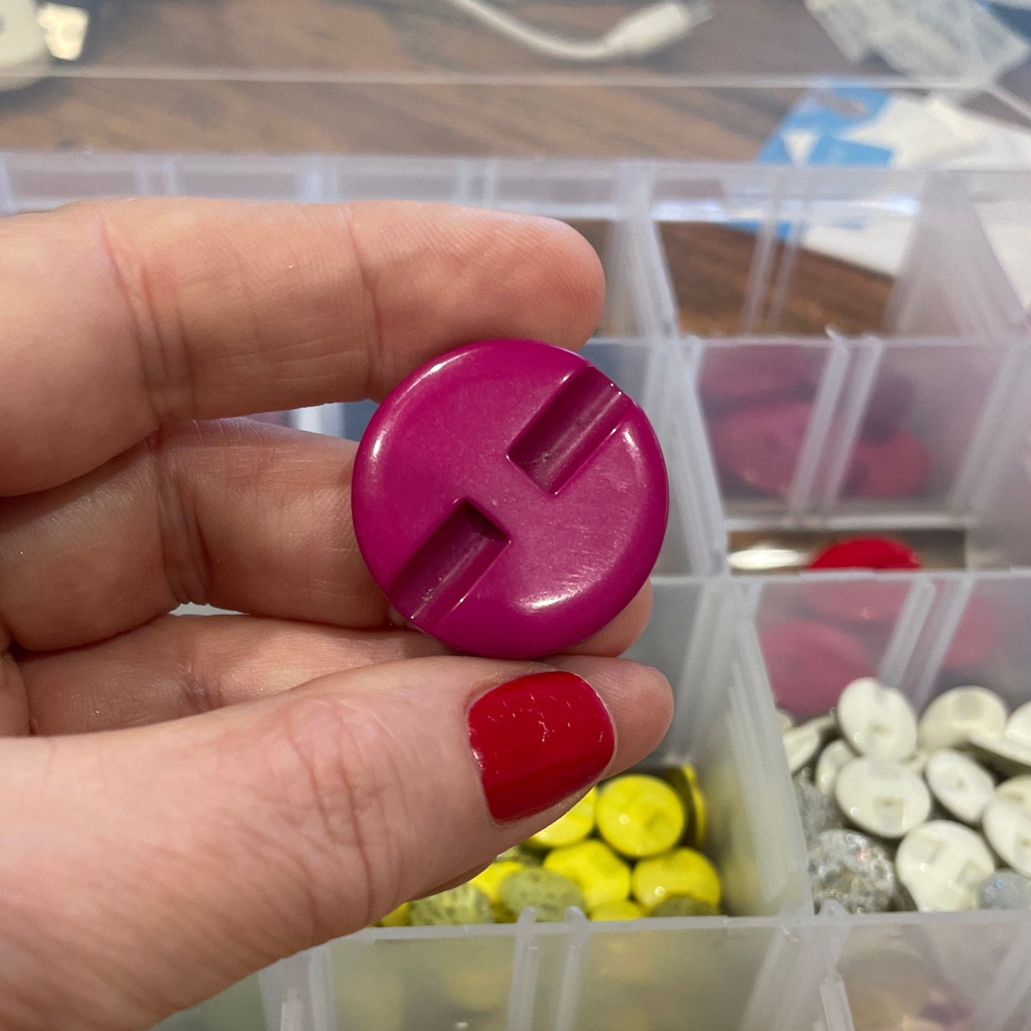 Hand holding a pink button with a container of colorful buttons in the background