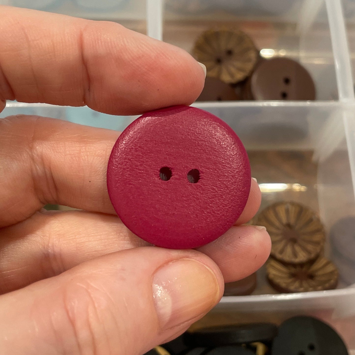 Hand holding a red button with a clear container of assorted buttons in the background