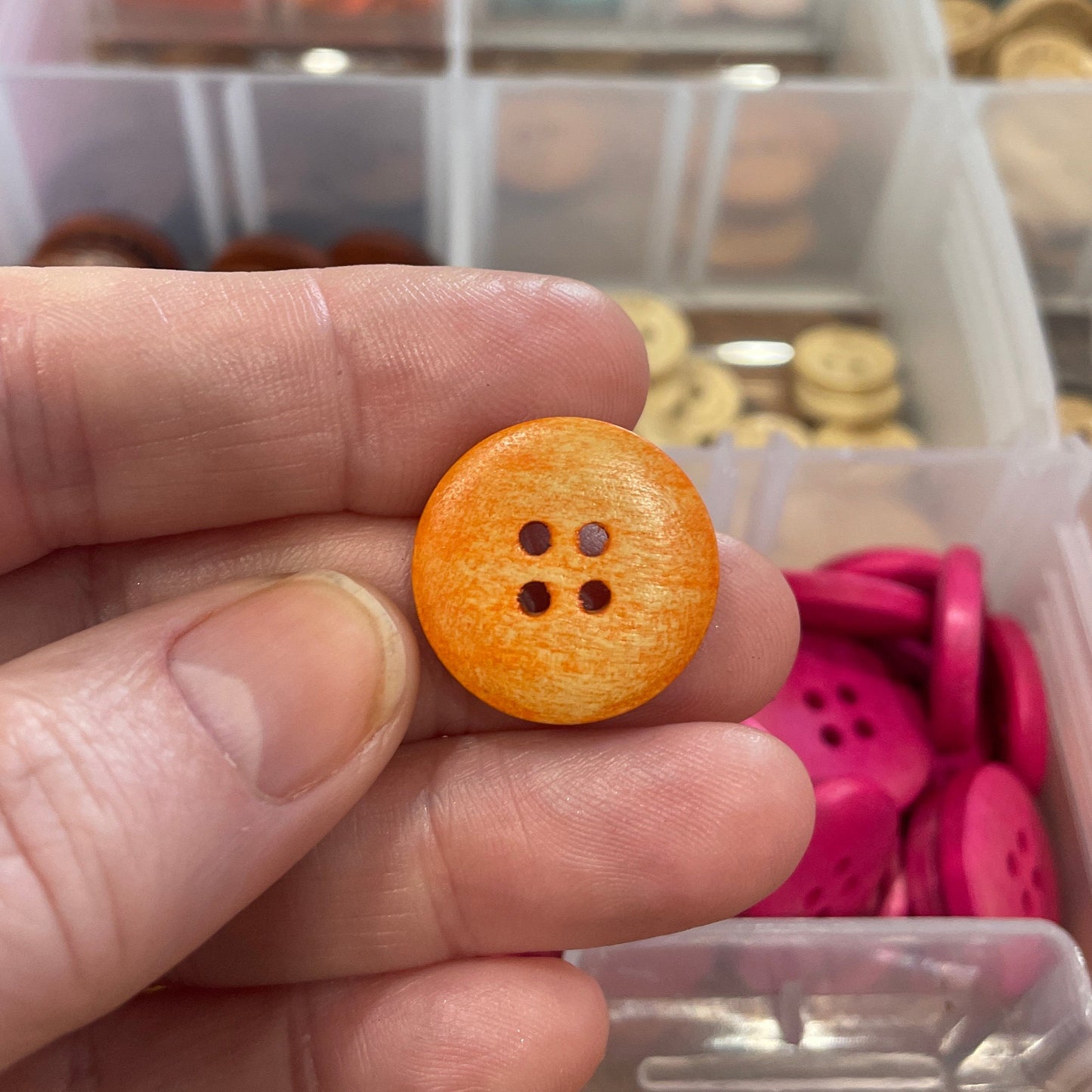 Hand holding a yellow button with a container of buttons in the background
