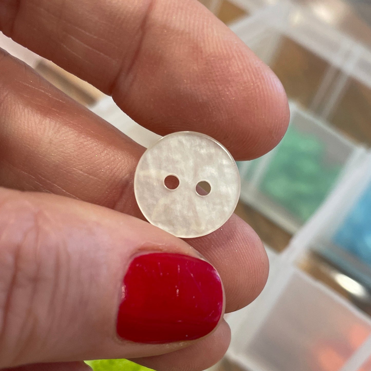 Hand holding a white button with a blurred background of a button organizer.