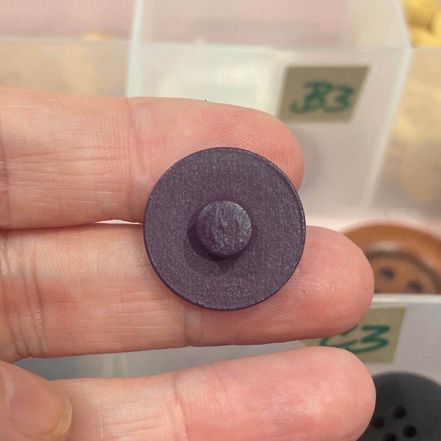 Purple button held between fingers with a background of various buttons