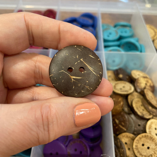 Hand holding a decorative button with a background of assorted buttons in a container.