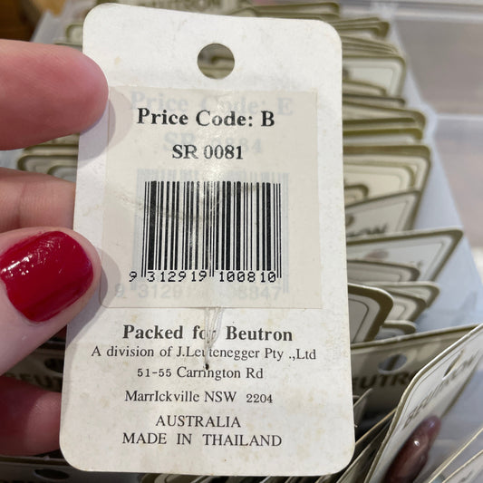 Close-up of a product tag with a barcode and text, held by a hand with red nail polish.