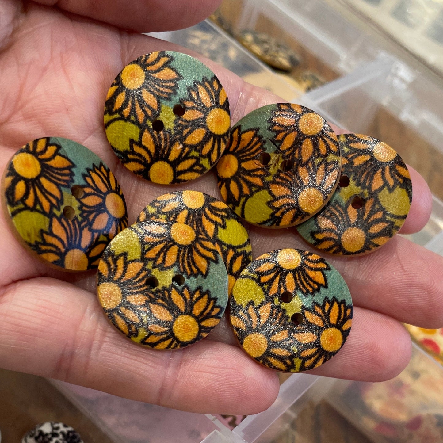 Hand holding floral-patterned buttons with a container of assorted buttons in the background.
