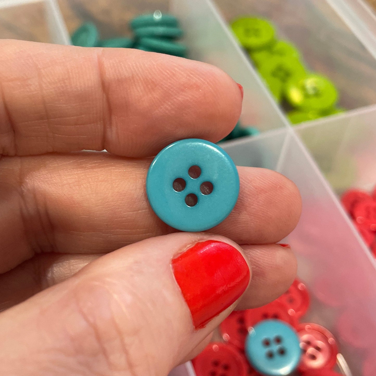 Hand holding a blue button with a container of buttons in the background