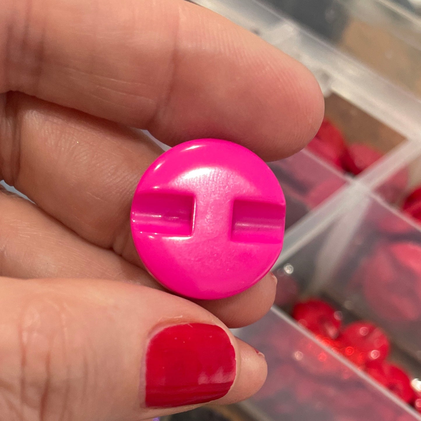 Hand holding a pink button, surrounded by various colored buttons in a clear container.