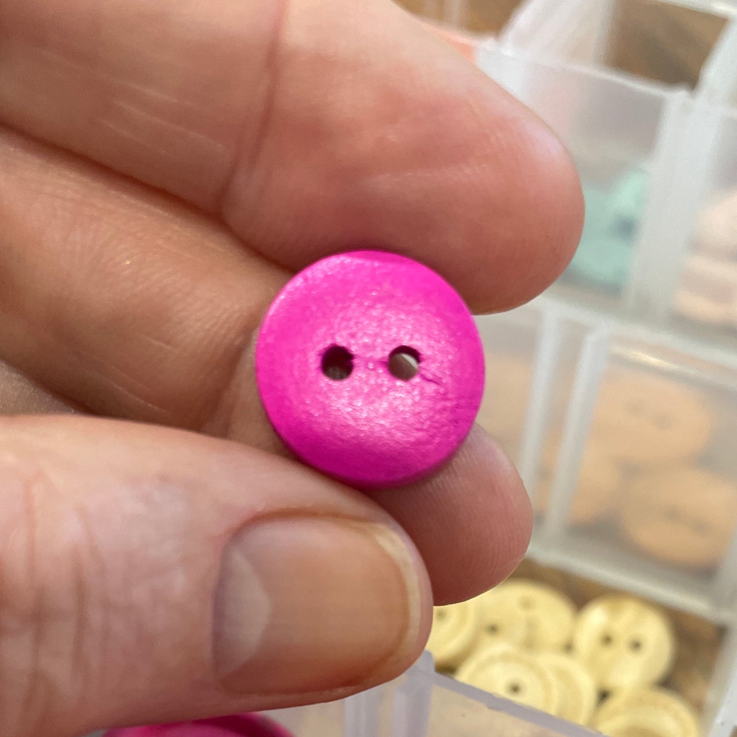Pink button held by a hand with a container of pink buttons in the background