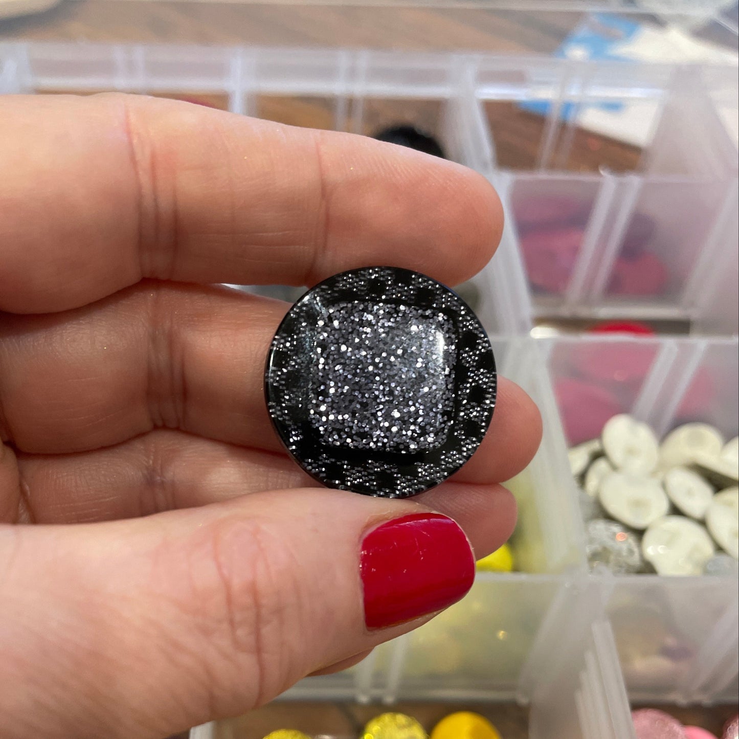 Hand holding a black glittery gemstone with a container of colorful gemstones in the background.