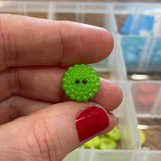 Hand holding a green button with a blurred background of button assortment