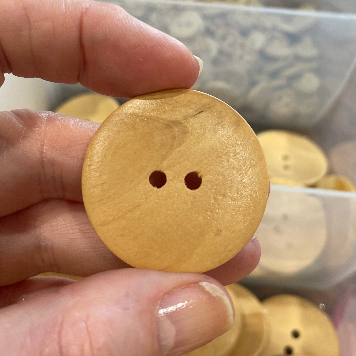 Hand holding a wooden button with a clear container of buttons in the background